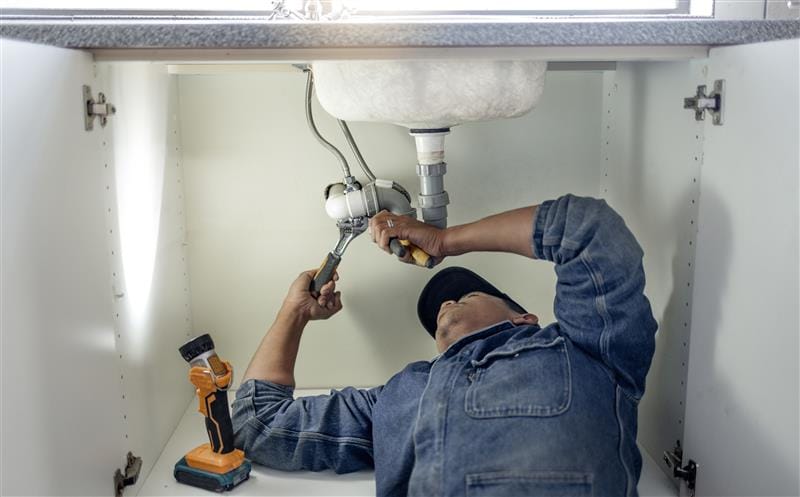 Plumber repairing pipes beneath a bathroom sink in Rancho Cucamonga