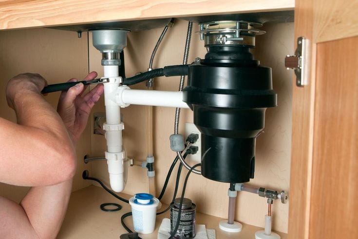 Plumber installing a garbage disposal beneath a kitchen sink in Rancho Cucamonga