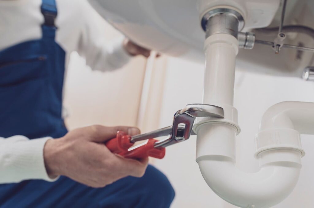 Plumber repairing a white drain pipe beneath a sink in Rancho Cucamonga