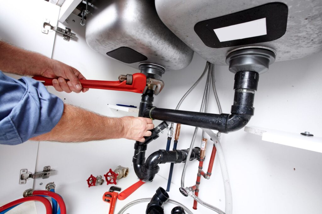 Plumber repairing drain pipes beneath a kitchen sink in Rancho Cucamonga